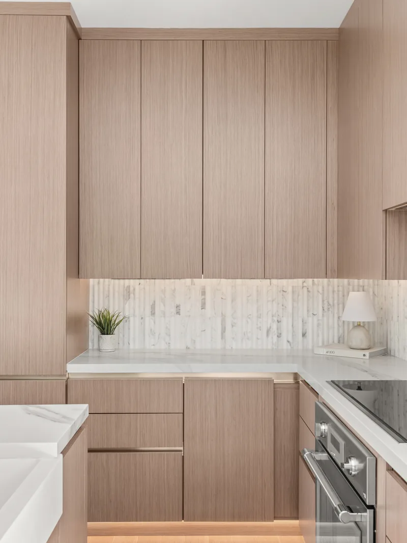 The perimeter run at completion: induction cooktop, single electric wall oven, and a stacked-mosaic backsplash under lit uppers