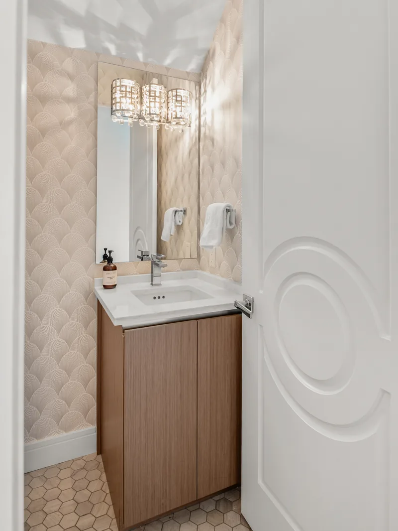 The powder bath after its change order: a new wood-grain vanity and mirror under a crystal light, quilted wallcovering, and the existing sink reset in place