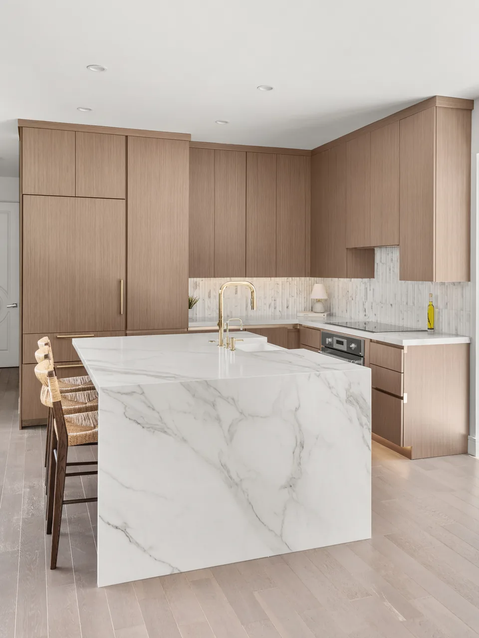 The same view at completion: a marble-veined quartz island with a waterfall edge and brass faucet below floor-to-ceiling wood-grain cabinetry