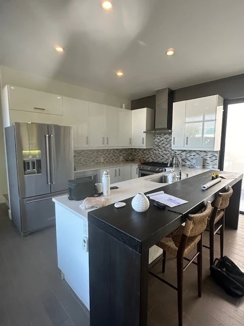 Consult-day phone snapshot of the Winter Park kitchen before remodeling: glossy white flat-panel cabinets, a stainless refrigerator, and a raised black bar-height seating wall on the island