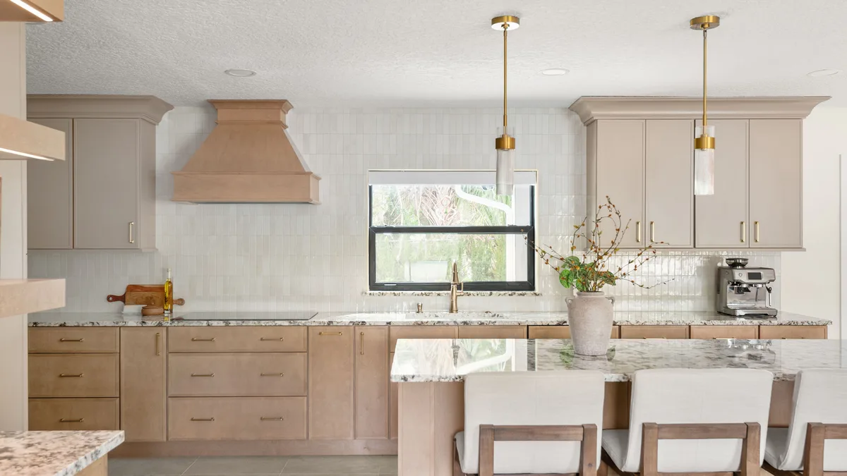 The remodeled Winter Park kitchen: light-oak cabinets under brass pendants, a wood range hood on white tile, and a stone-topped island with white counter stools