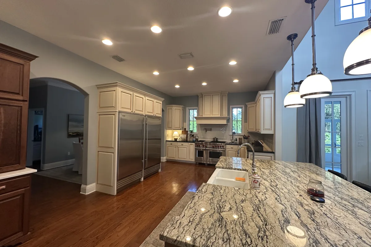 The DeLand kitchen before remodeling: glazed raised-panel cabinets, a patterned granite island, and pendant lights under the two-story ceiling