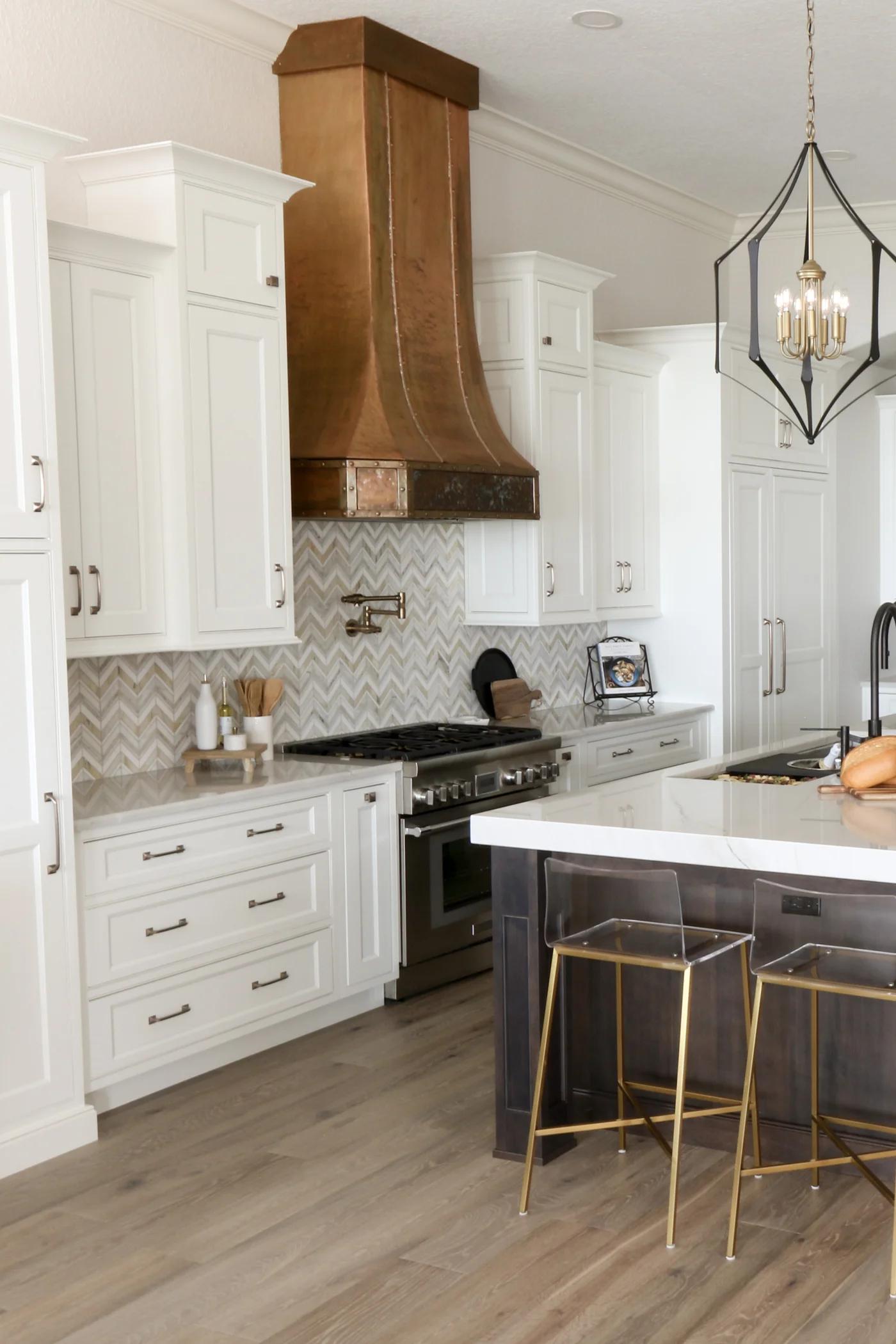 Windermere estate kitchen remodel — the hammered bronze range hood over the chevron marble backsplash and professional range