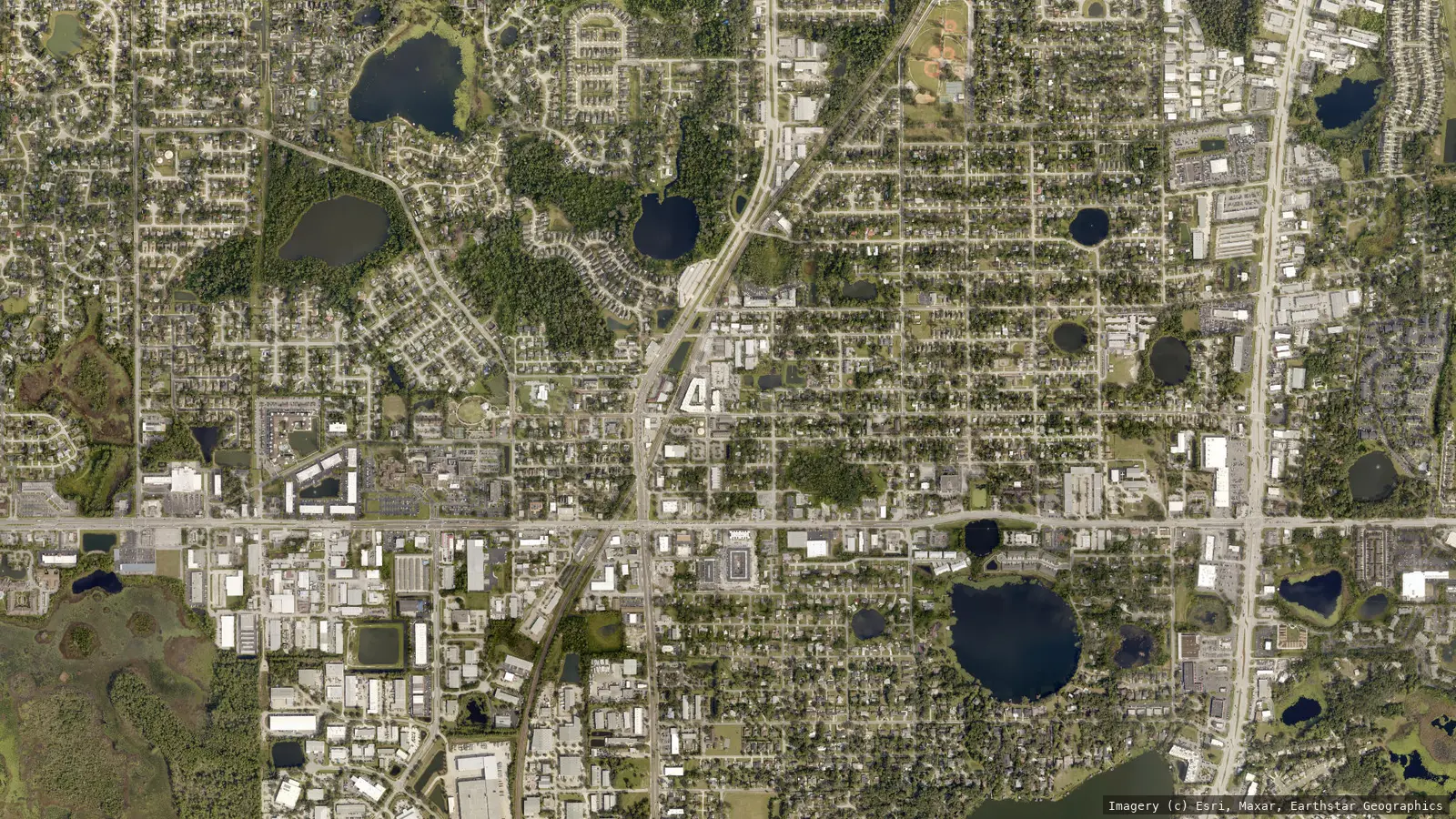 Satellite view of Longwood, Florida from neighborhood altitude &mdash; the historic district street grid, the SunRail corridor, lakes and tree canopy. Imagery &copy; Esri, Maxar, Earthstar Geographics