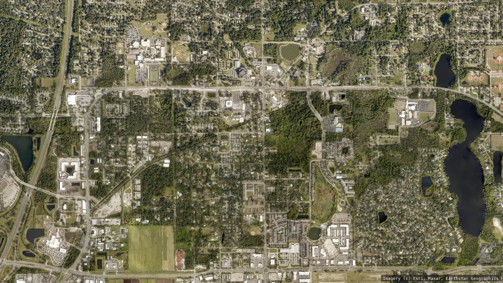 Satellite view of Oviedo, Florida from neighborhood altitude &mdash; the downtown crossing, tree canopy, lakes and master-planned subdivisions. Imagery &copy; Esri, Maxar, Earthstar Geographics