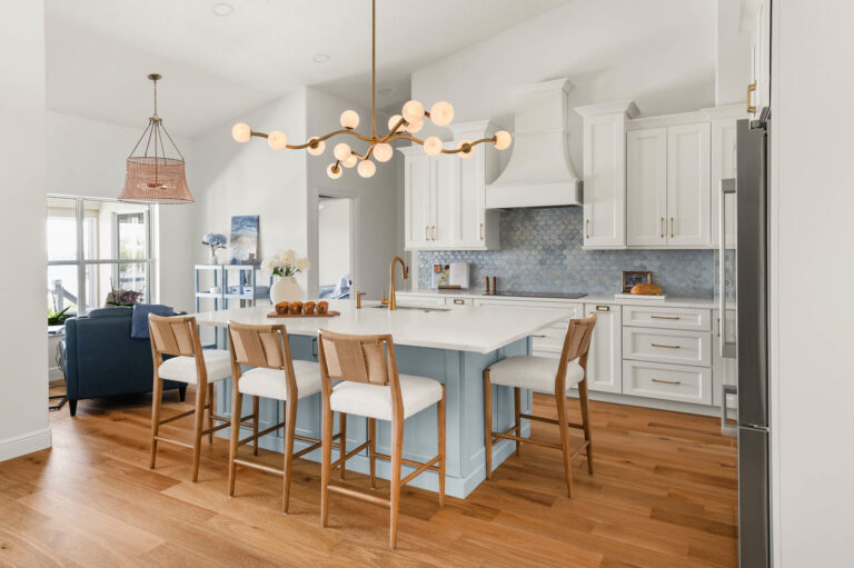 Remodeled Clermont FL lakefront kitchen with white cabinetry, a soft blue island, brass chandelier and wide-plank wood floors