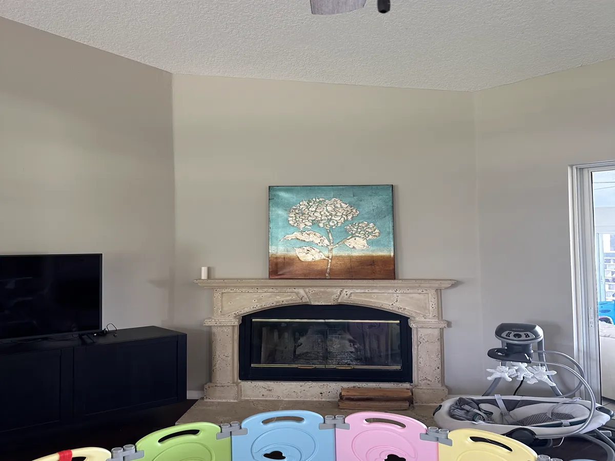 The family room before remodeling: a corner fireplace with a cast stone arched surround and mantel shelf, brass-trimmed glass doors, and beige walls