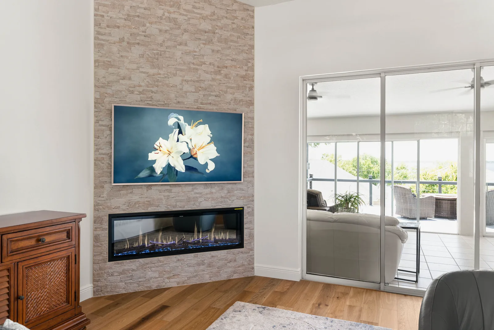 The family room new stacked stone fireplace wall with a linear firebox and a framed art panel above, beside sliding doors to the screened balcony