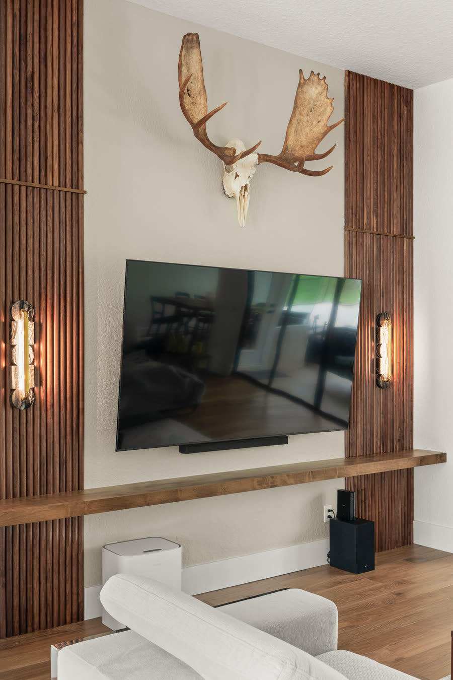 Remodeled Orlando entertainment wall with dark-stained slatted wood panels flanking a wall-mounted television, a full-width wood shelf and two vertical sconces