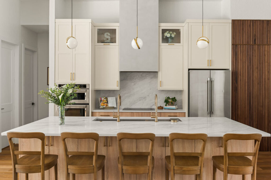 Remodeled Orlando kitchen island under three brass and glass globe pendants, with cream cabinetry, a pale veined slab backsplash and built-in wall ovens