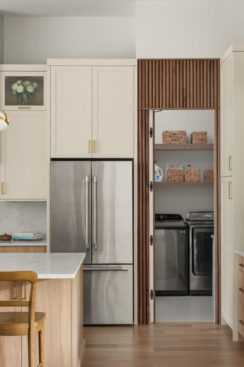 Dark-stained slatted wood doors beside the refrigerator, open to reveal a concealed laundry room with a washer, dryer and open shelving