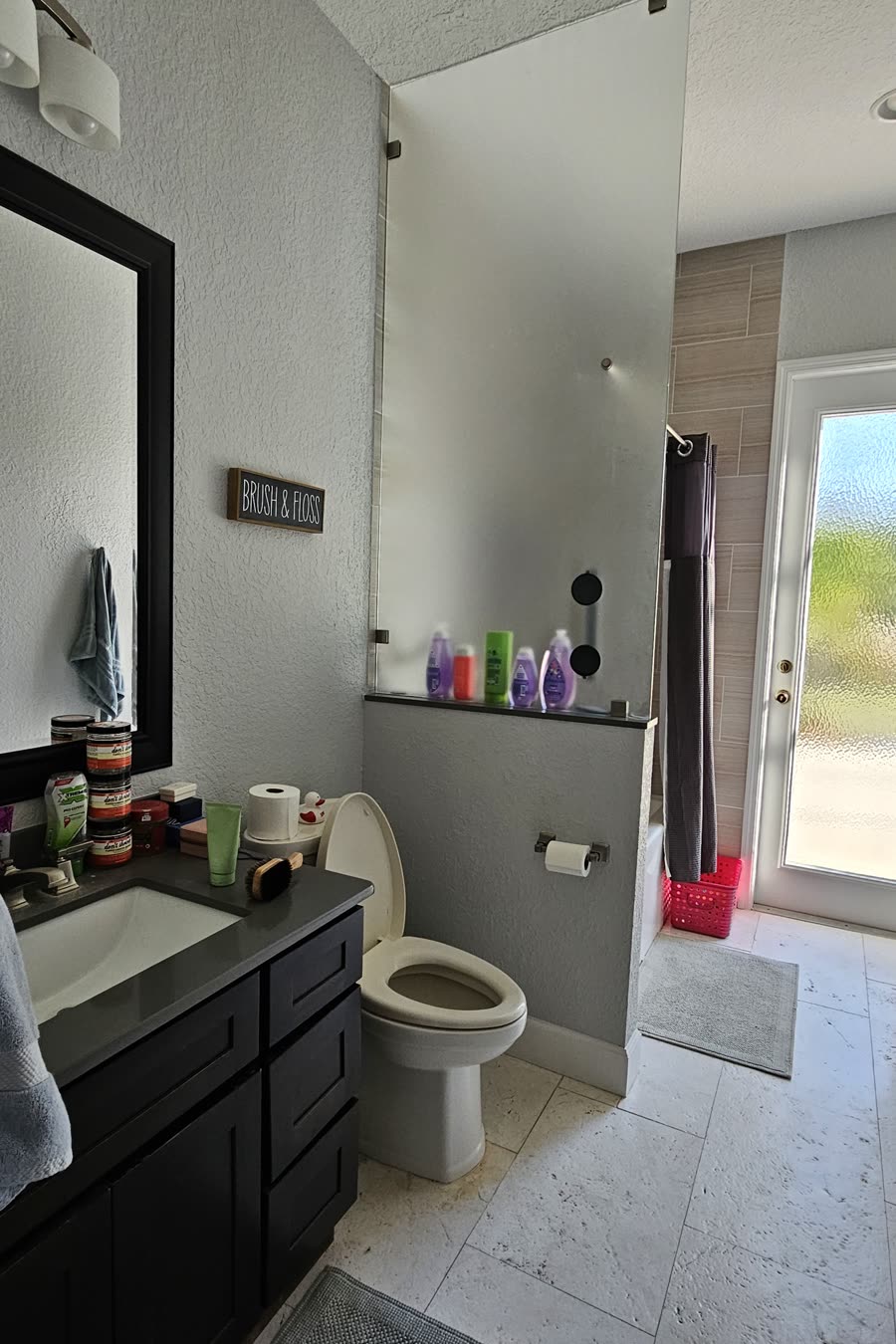 Orlando pool bathroom before remodeling, with a dark vanity and counter, a framed mirror and a tub-shower behind a curtain beside the pool door