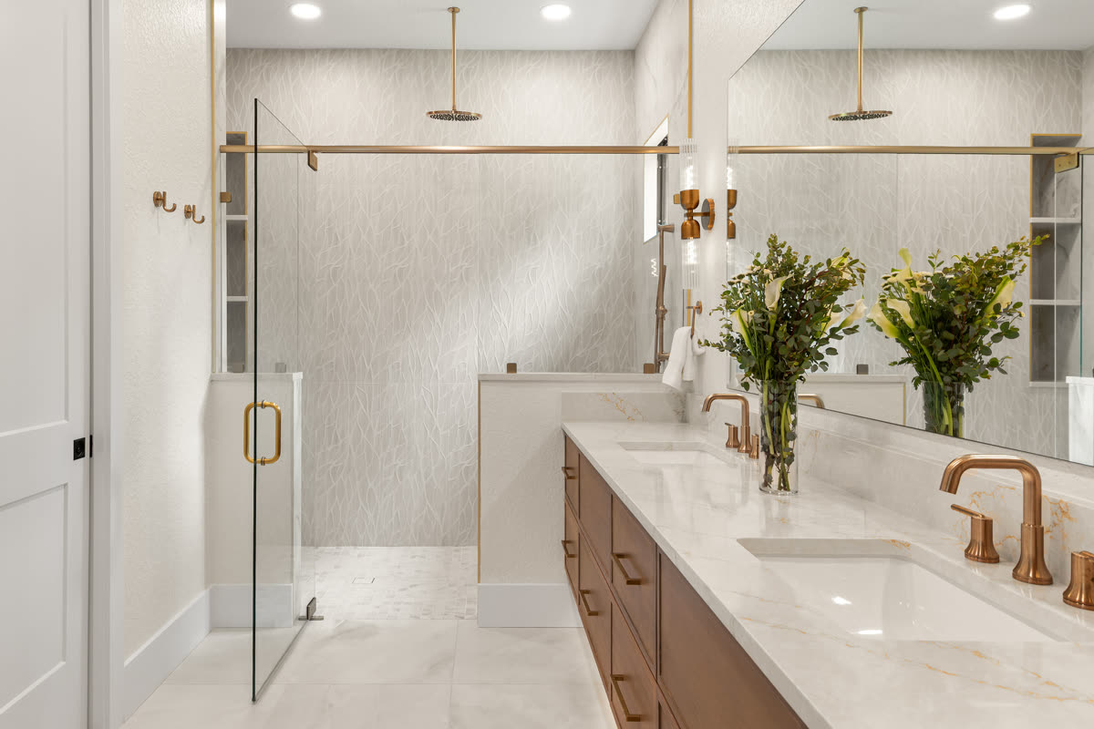 Remodeled Orlando primary bathroom with a floating wood double vanity, pale slab counter, brass fixtures and a walk-in shower behind a glass panel
