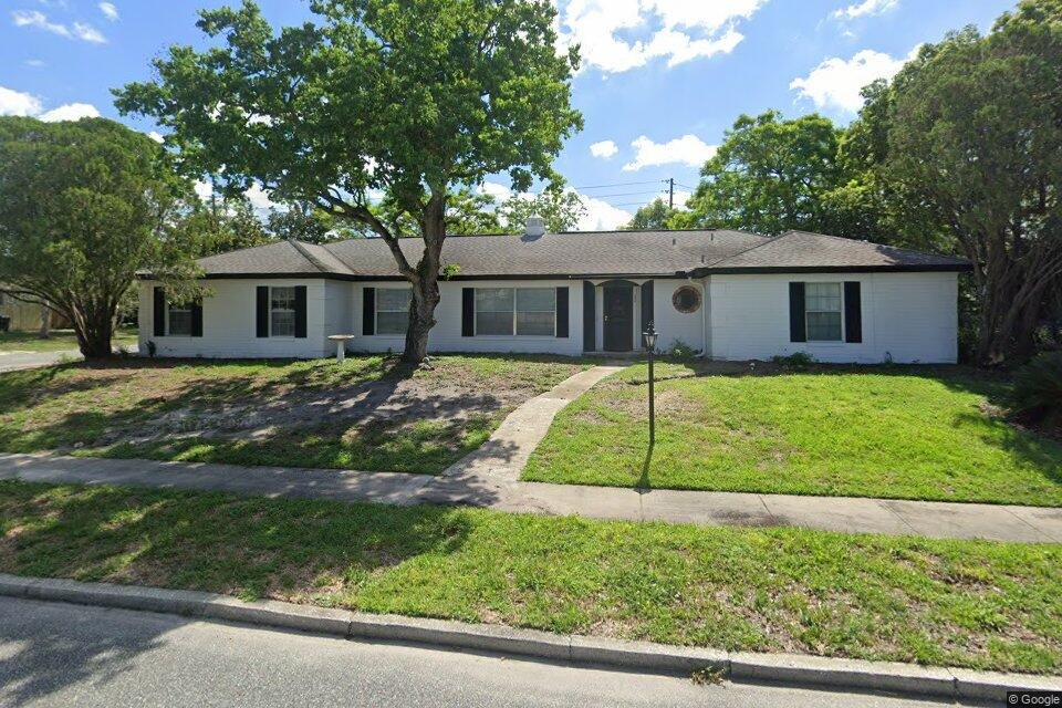 The front of the Winter Park home before the renovation, captured from the street: a white single-story house with black shutters, a bare front yard and a large oak over the walk (Google Street View image)