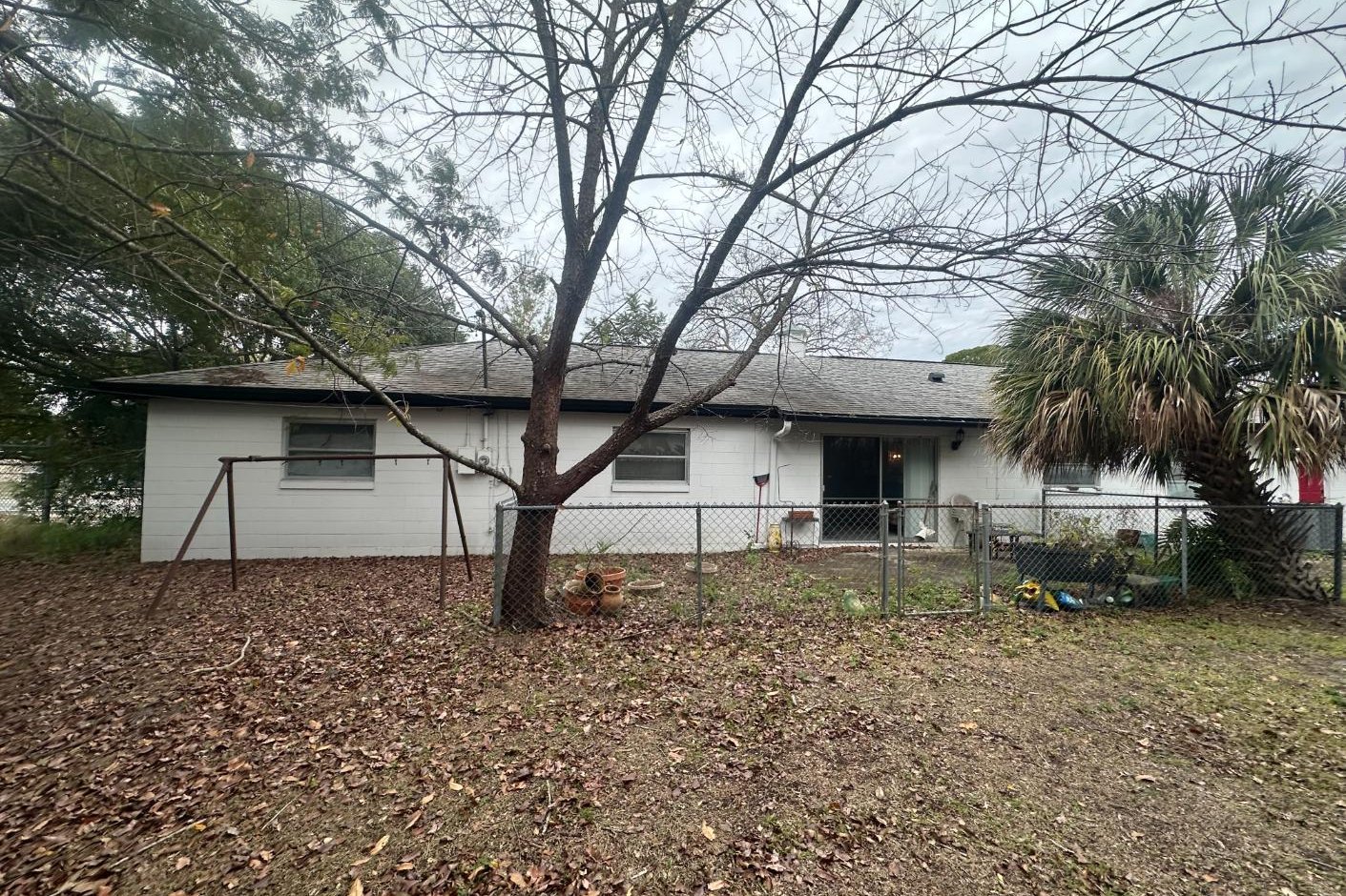 The rear of the Winter Park home before the renovation: painted block walls, a chain-link fence, bare ground and a single sliding door where the screened lanai now stands