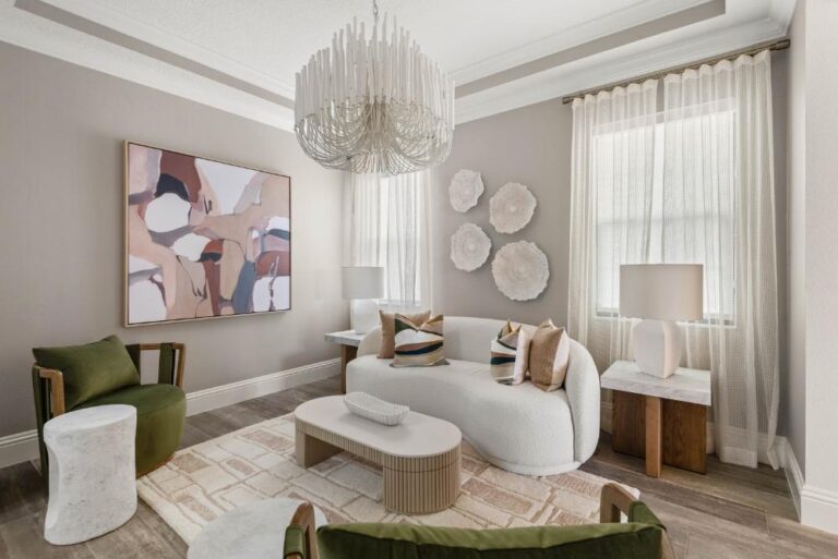 A sitting room from a KBF Design Gallery interior design project in Maitland: a curved white textured sofa under a white beaded chandelier, a large abstract painting, wall-mounted white sculptural discs, sheer drapery, marble-topped side tables, a fluted oval coffee table and green velvet armchairs on a cream patterned rug